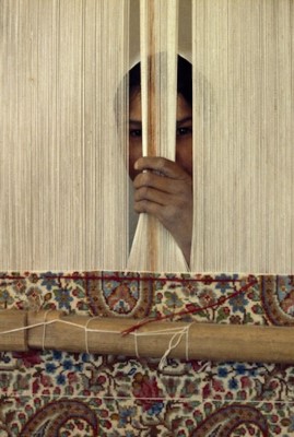 irl peeks through cotton cords on a loom at a rug factory - Kerman -