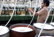 کارگر کارخانه نساجی ایران در کنار ماشینآلات تولید نخ و الیاف؛ صنعت نساجی و چالش هزینههای تولید داخلی.